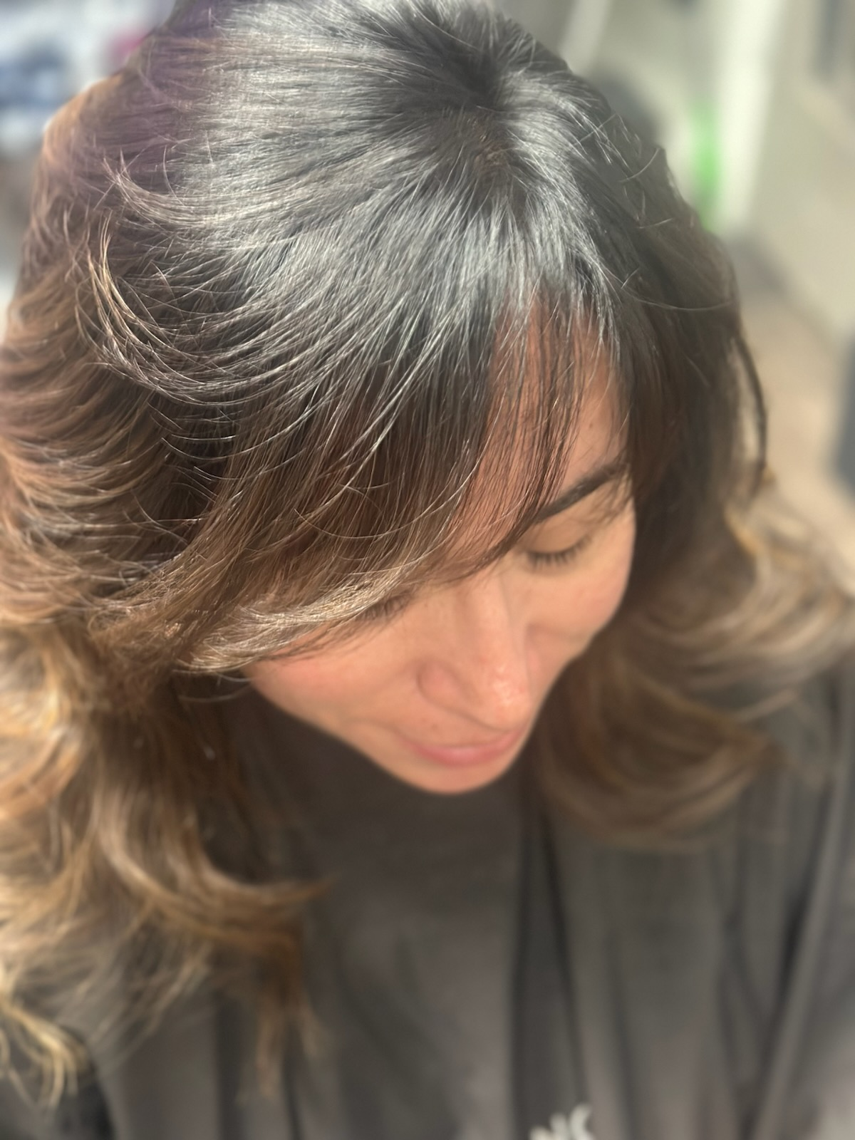 Overhead view of a person with dark wavy hair in a black top, looking downward in soft light