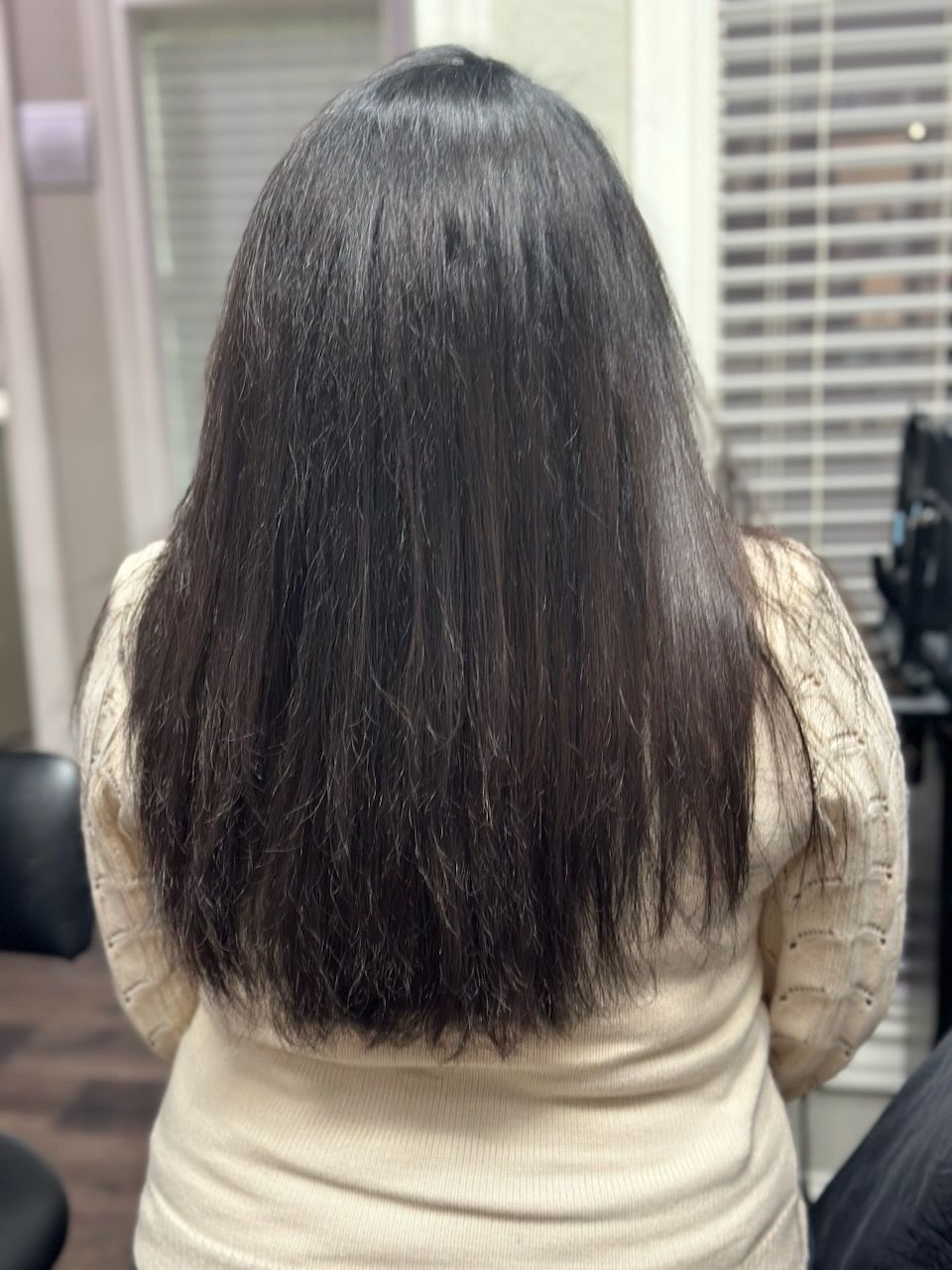 Back view of a person with long black hair wearing a beige sweater indoors