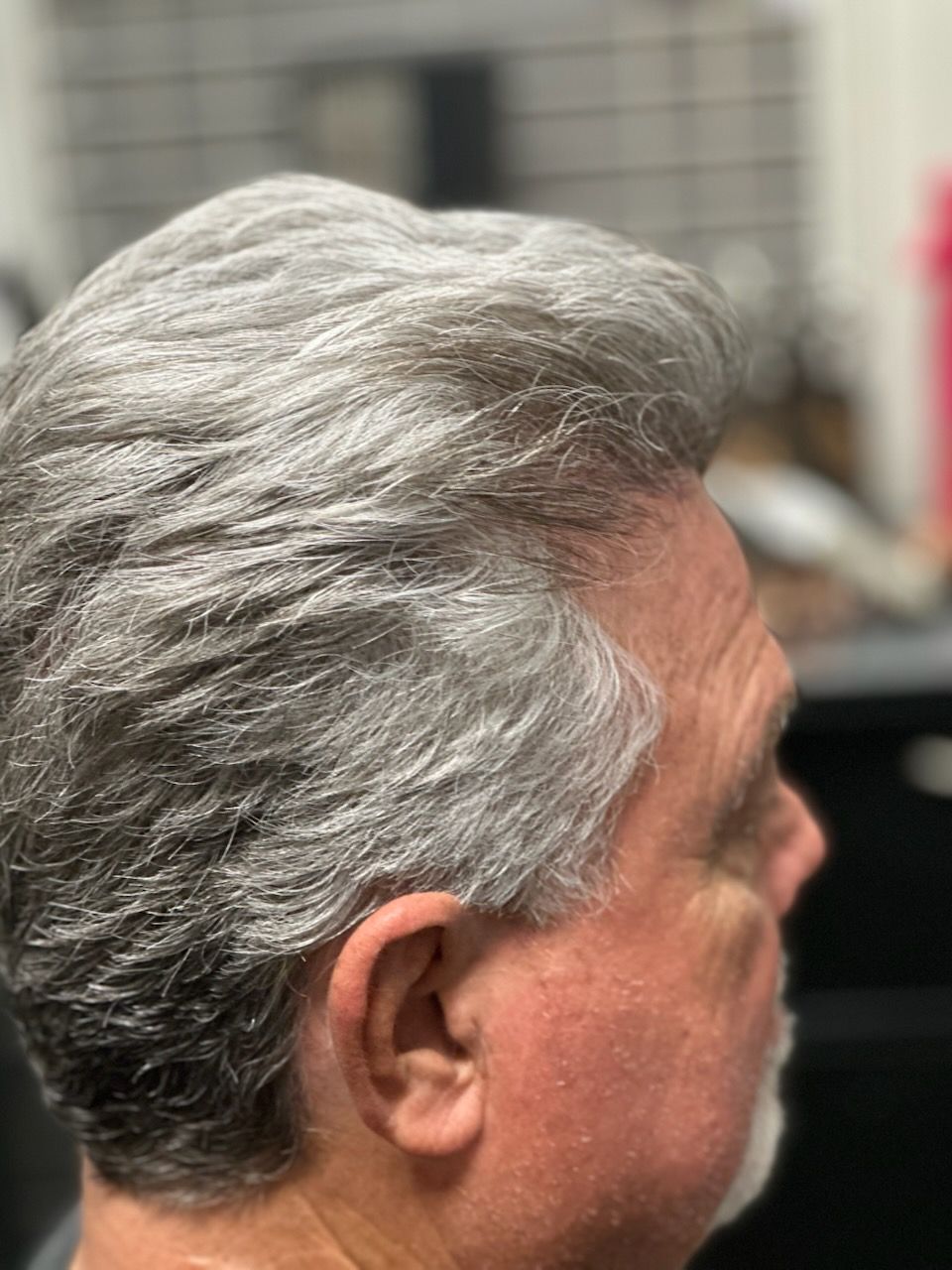 Side profile of a man with gray hair in a blurred indoor setting