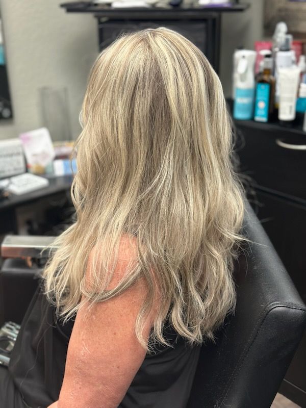 Blonde wavy hair with soft highlights in a salon chair, viewed from behind.