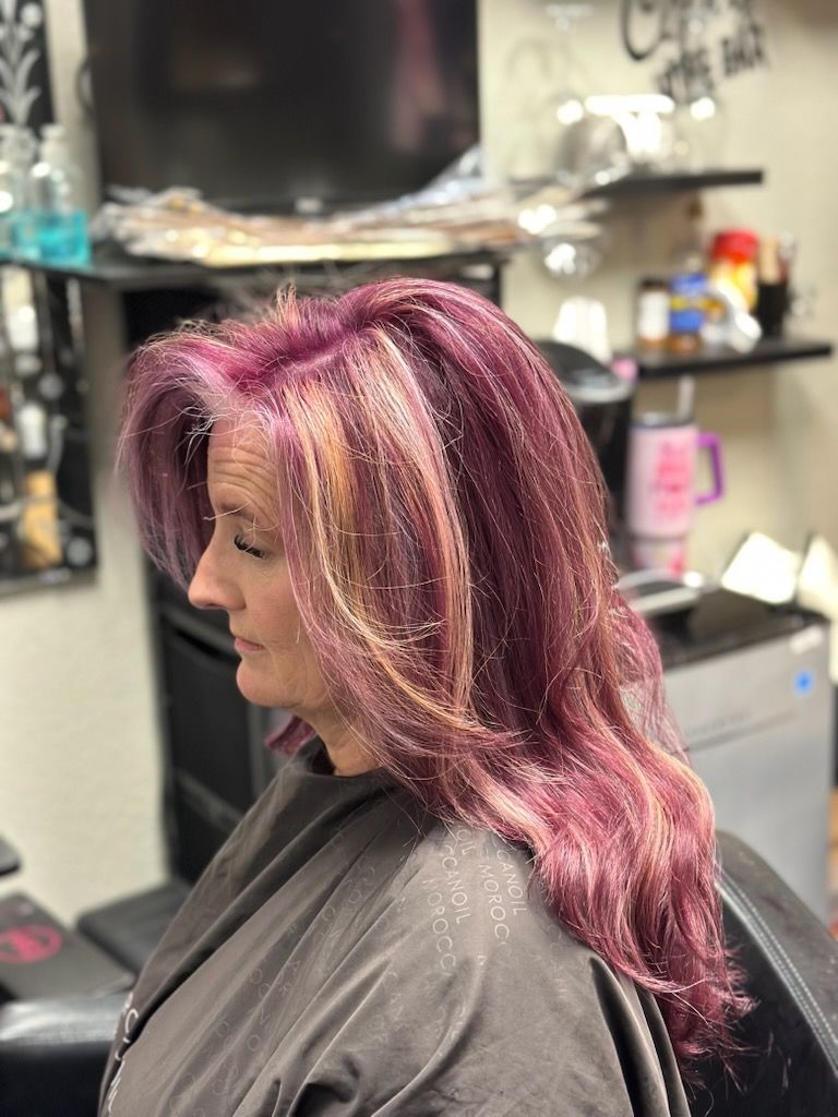 Side profile of a person with long pink hair in a salon chair, with hair products visible in the background.