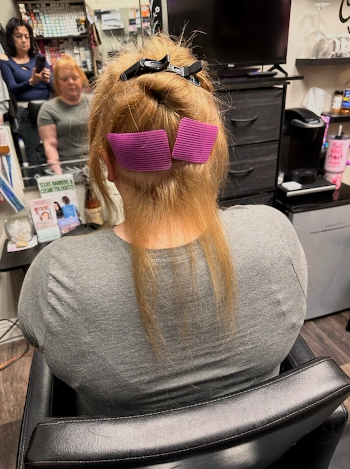 Salon chair with blonde hair being sectioned and clipped up with pink rollers or clips.