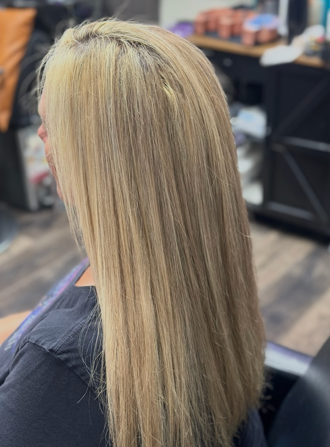 Side view of a blonde-haired person sitting in a salon chair with long straight hair