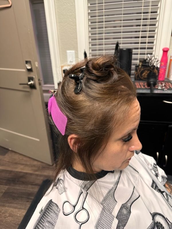 Girl in a salon chair with foil in her hair, wearing a cape, profile view.