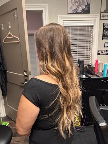 Person with long wavy hair sitting in a salon chair, viewed from behind, with a mirror and hair products nearby