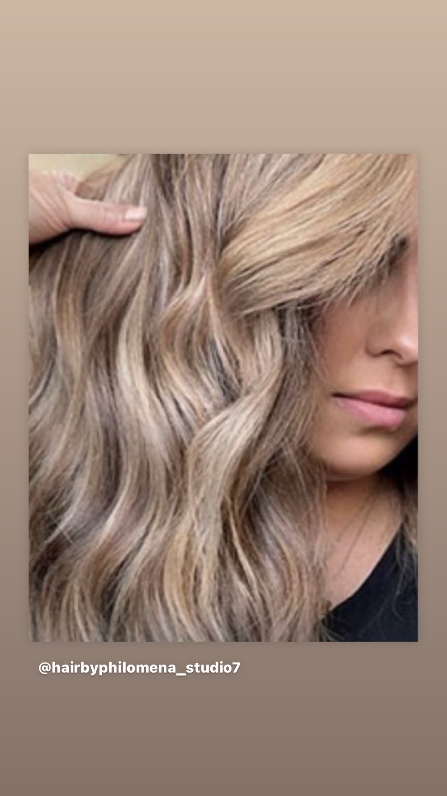 Close-up of wavy beige-blonde hair with highlighted strands, gently held by a hand.