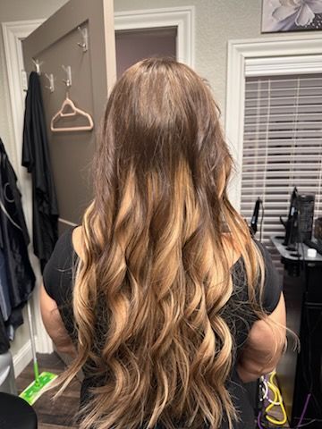 Person with long wavy brown hair standing indoors, viewed from behind, in a room with a closet and window blinds.