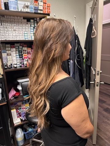 Woman with long wavy brown hair standing in a salon supply closet, viewed from the side.