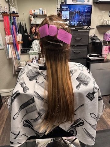 Salon chair with long straight hair clipped up in purple, cape draped over shoulders, and a TV in the background