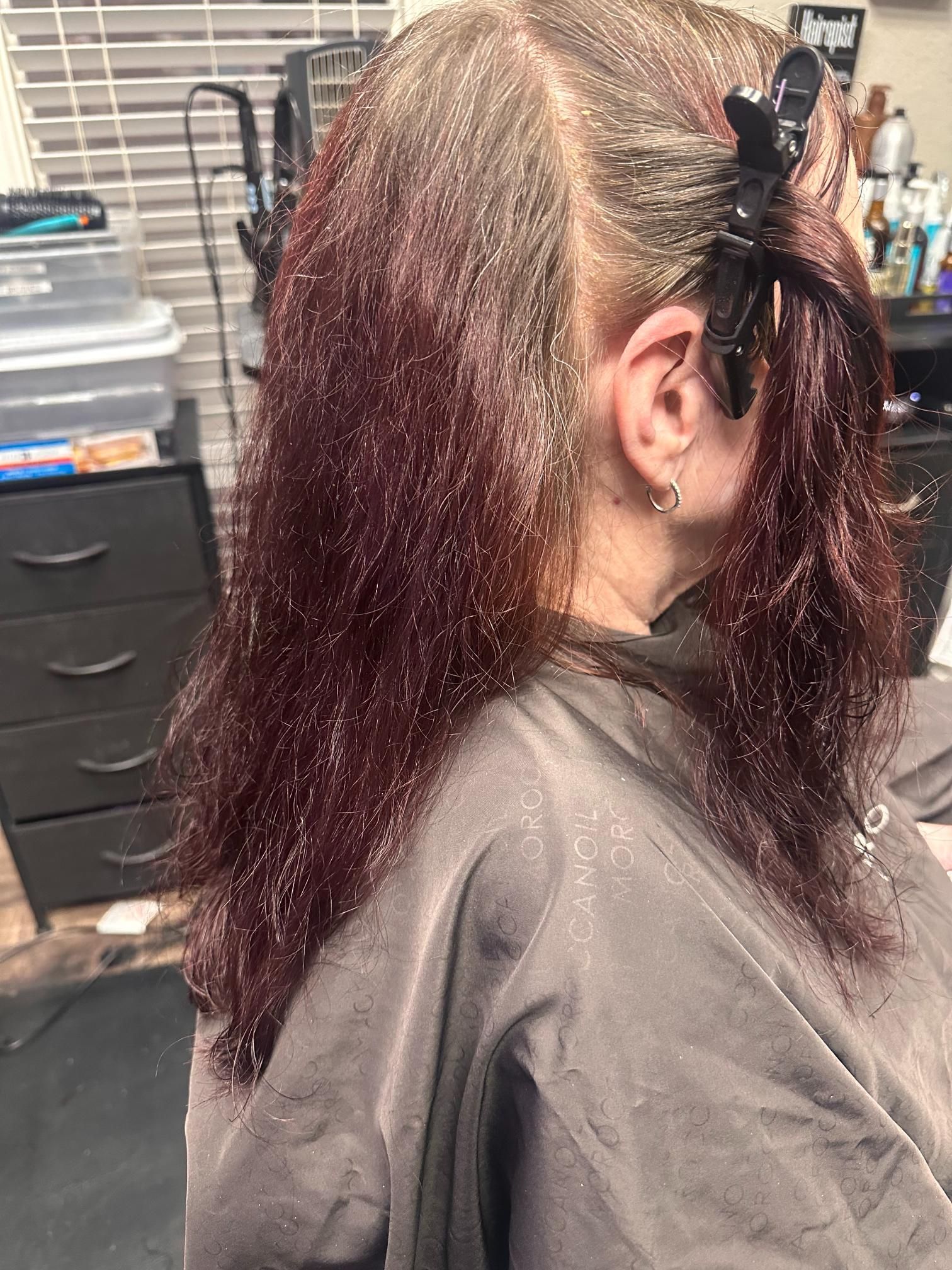 Client with long burgundy hair in a salon chair, sectioned with clips during a hairstyling session