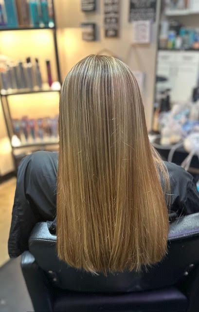 A woman with long blonde hair is sitting in a chair in a salon.