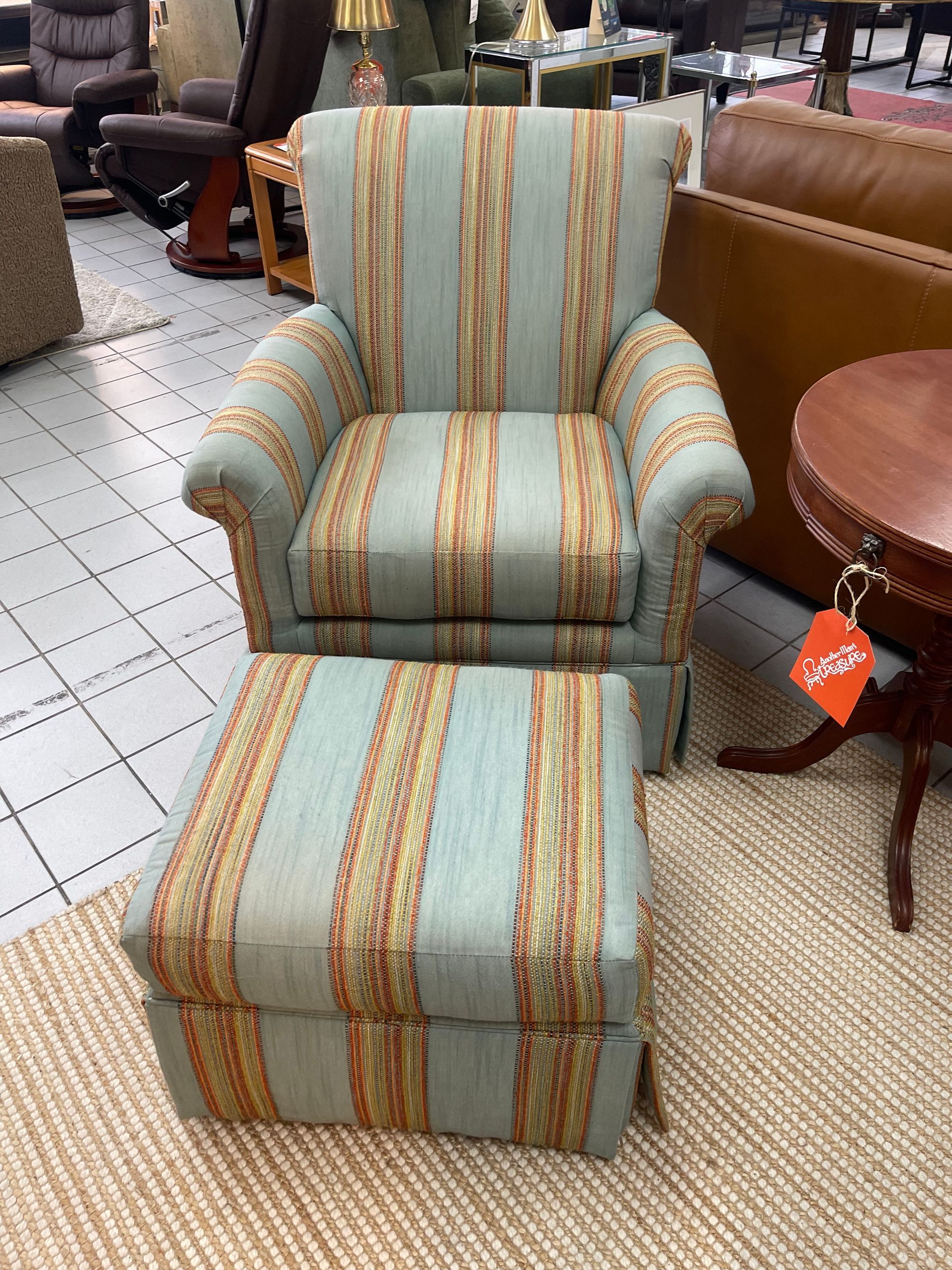 A blue and orange striped armchair with a matching ottoman, displayed on a rug in a furniture store.