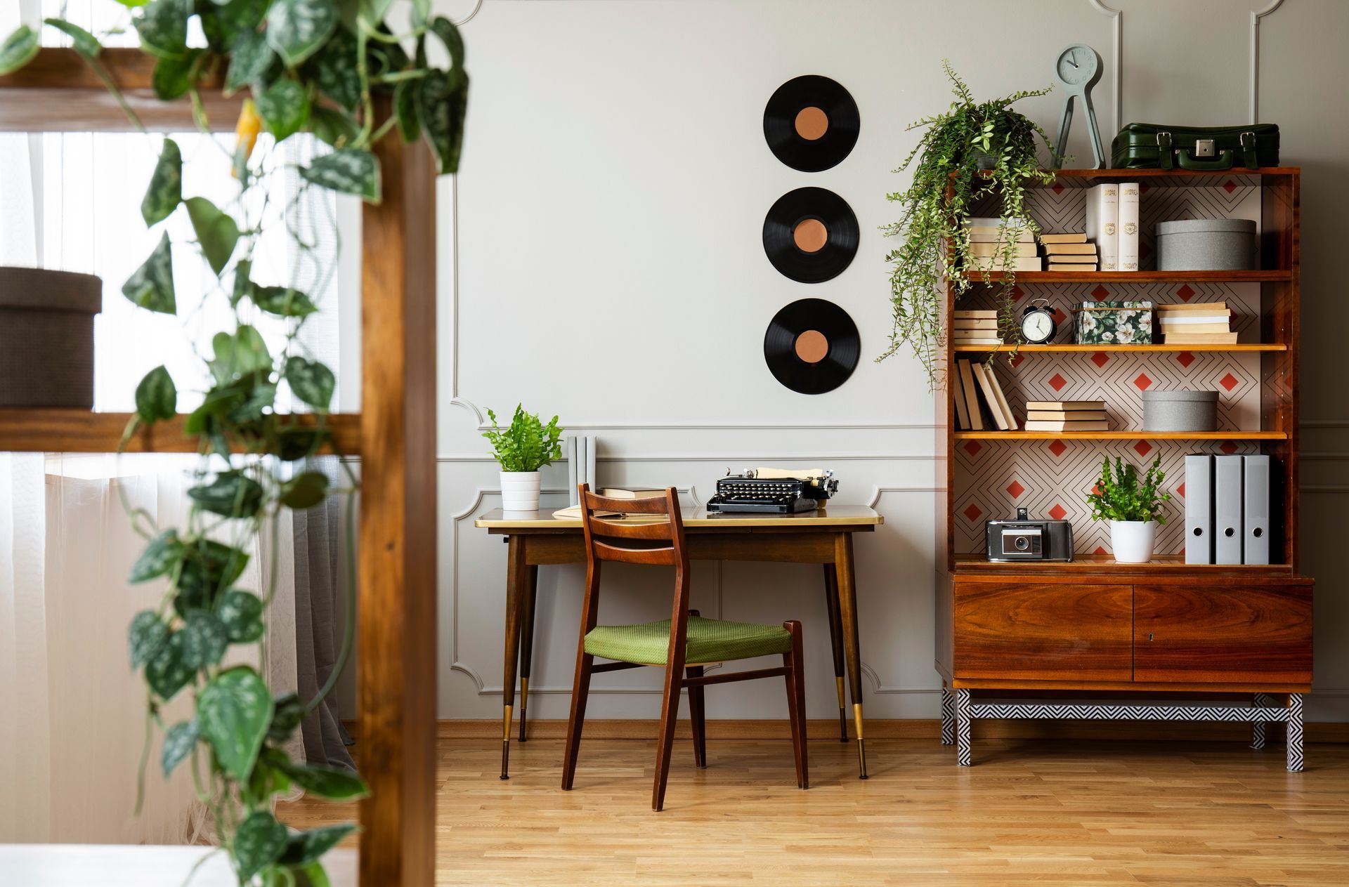 Black typewriter on a wood desk, a mid-century modern chair, and a bookcase