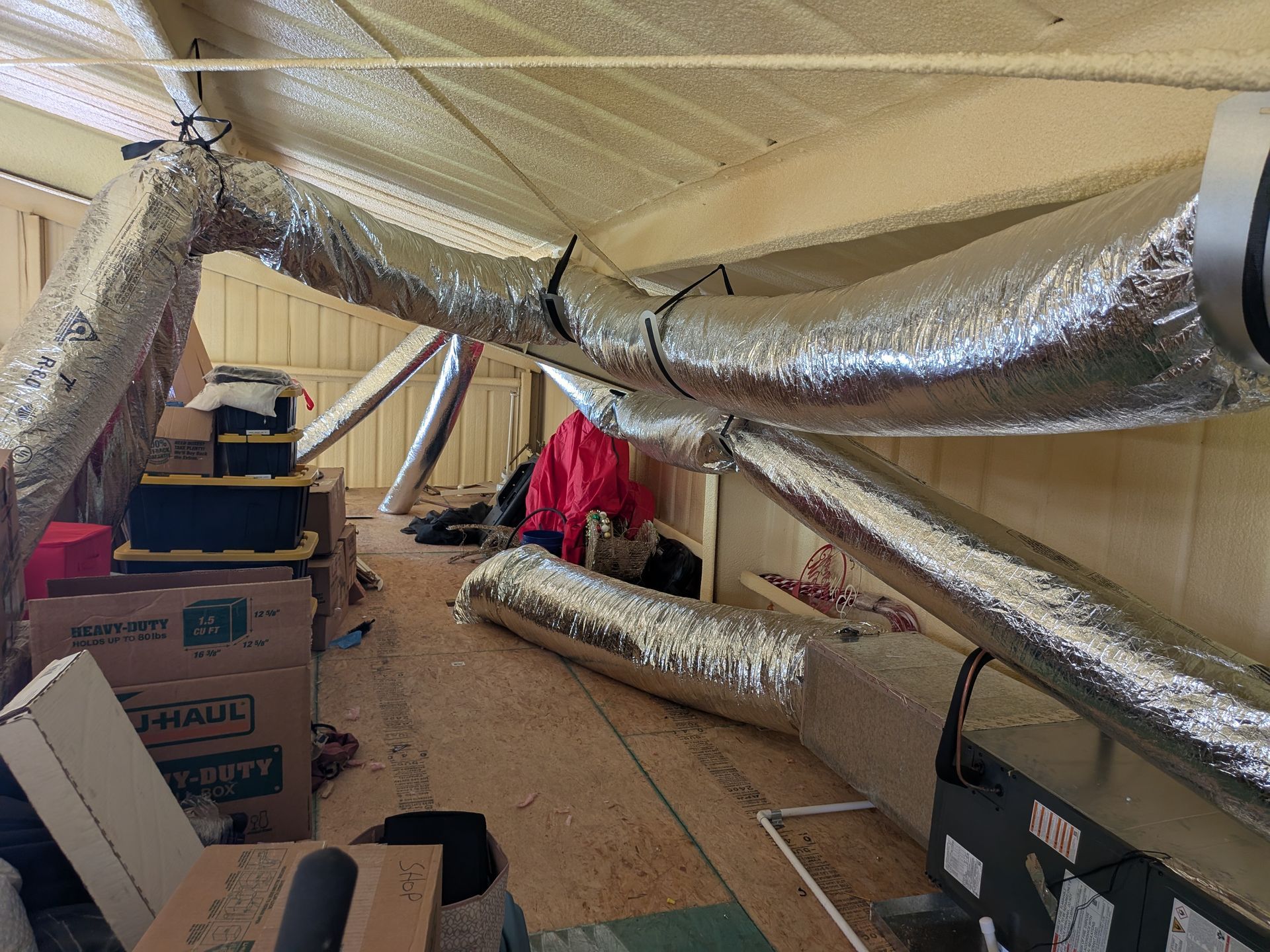 Attic interior with silver ductwork, boxes, and insulation.
