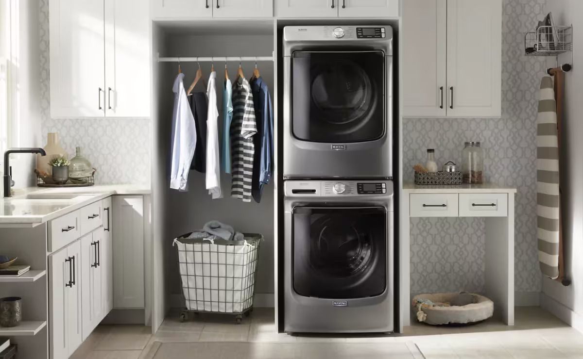 Laundry room with stacked washer and dryer, closet with hanging clothes, and a sink.