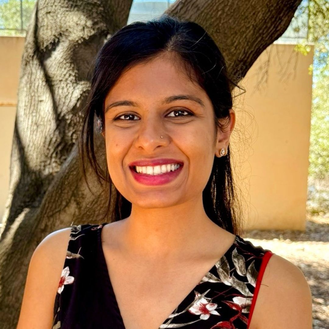 Woman with a nose ring smiling at the camera, in front of a tree.