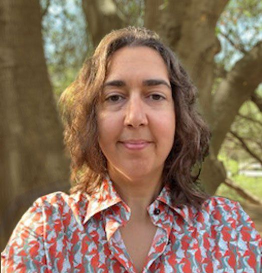 A woman in a colorful shirt is standing in front of a tree.