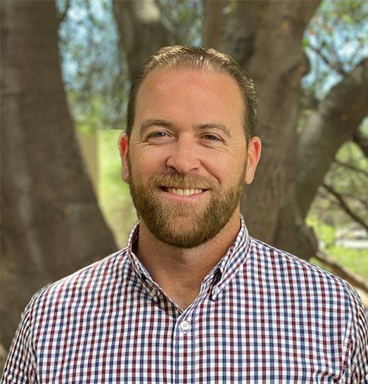 A man with a beard is wearing a plaid shirt and smiling for the camera.