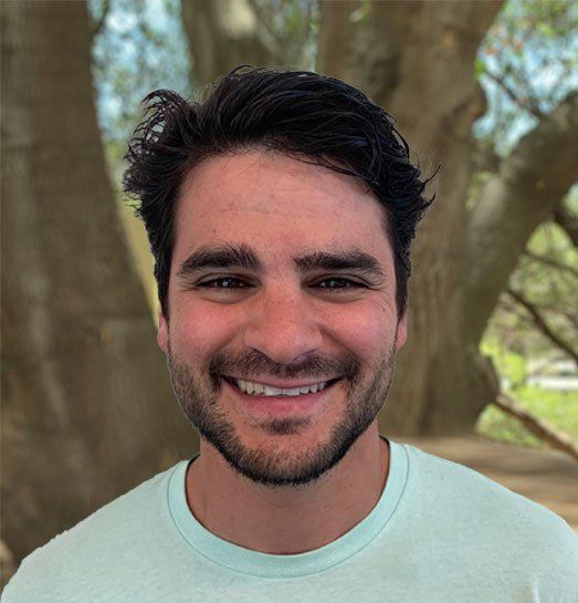A man with a beard is smiling in front of a tree.