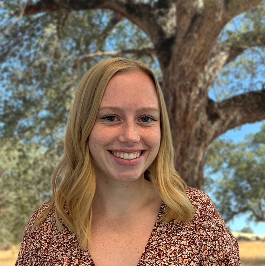 Woman with blonde hair smiling in front of a tree.