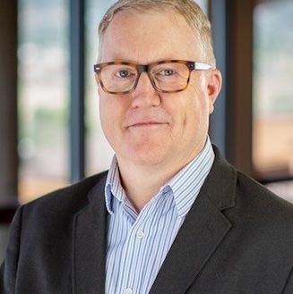 A man in a suit and plaid shirt is smiling for the camera.