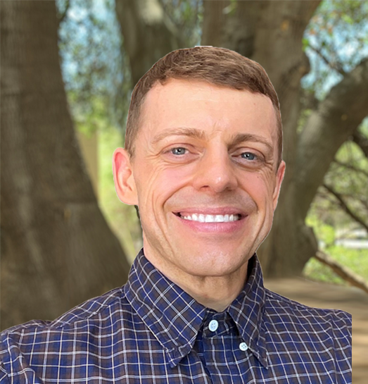 A man in a plaid shirt is smiling in front of a tree.