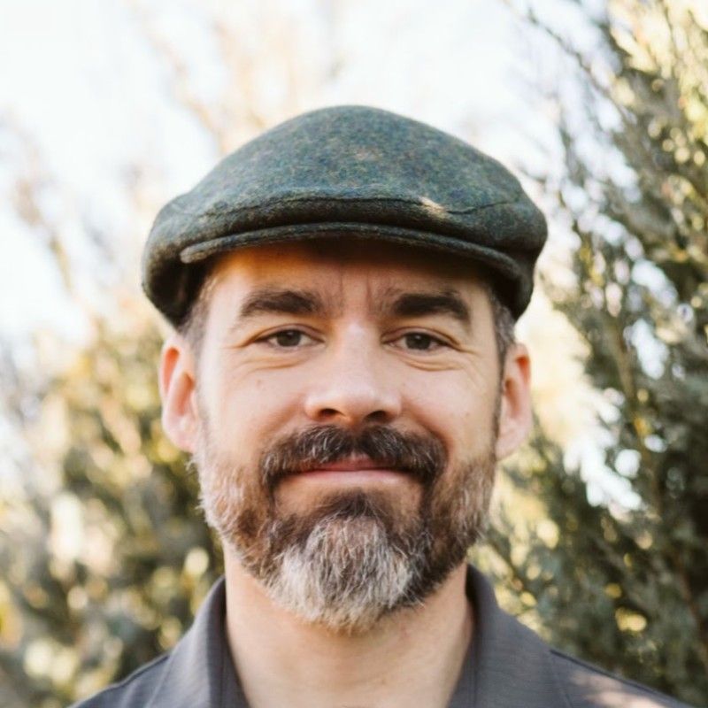 A man with a beard and hat is smiling for the camera.