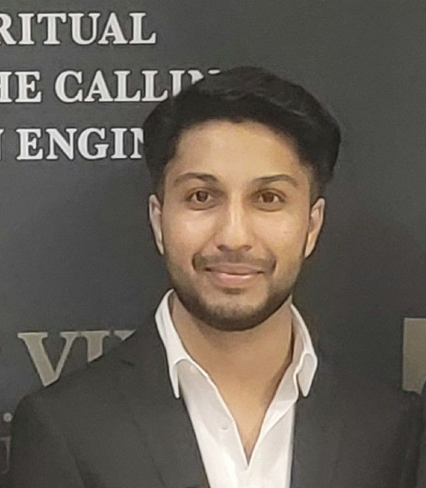 Man in a suit smiles, standing near a wall with text.