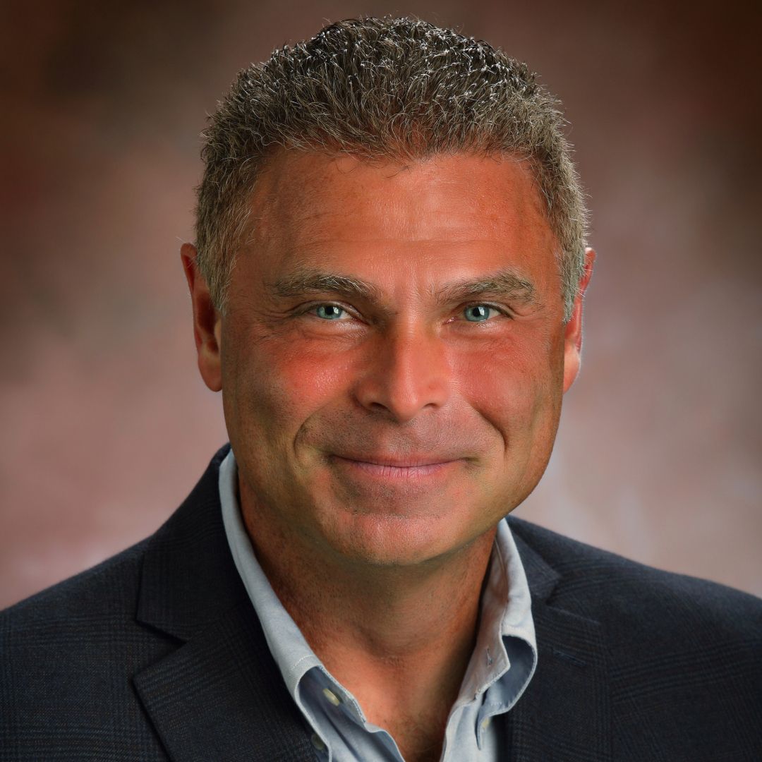 A man in a suit and plaid shirt is smiling for the camera.