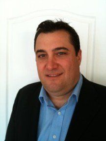 A man in a suit and blue shirt is smiling for the camera