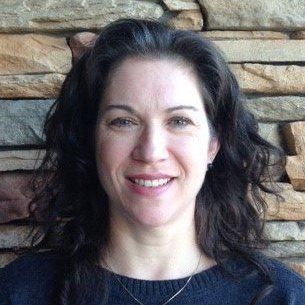A woman in a black sweater is smiling in front of a stone wall.