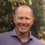 A man in a purple shirt is smiling for the camera.