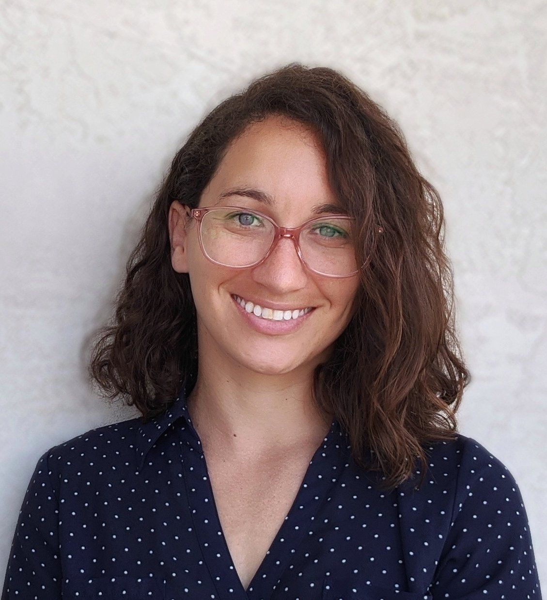 A woman wearing glasses and a polka dot shirt is smiling for the camera.