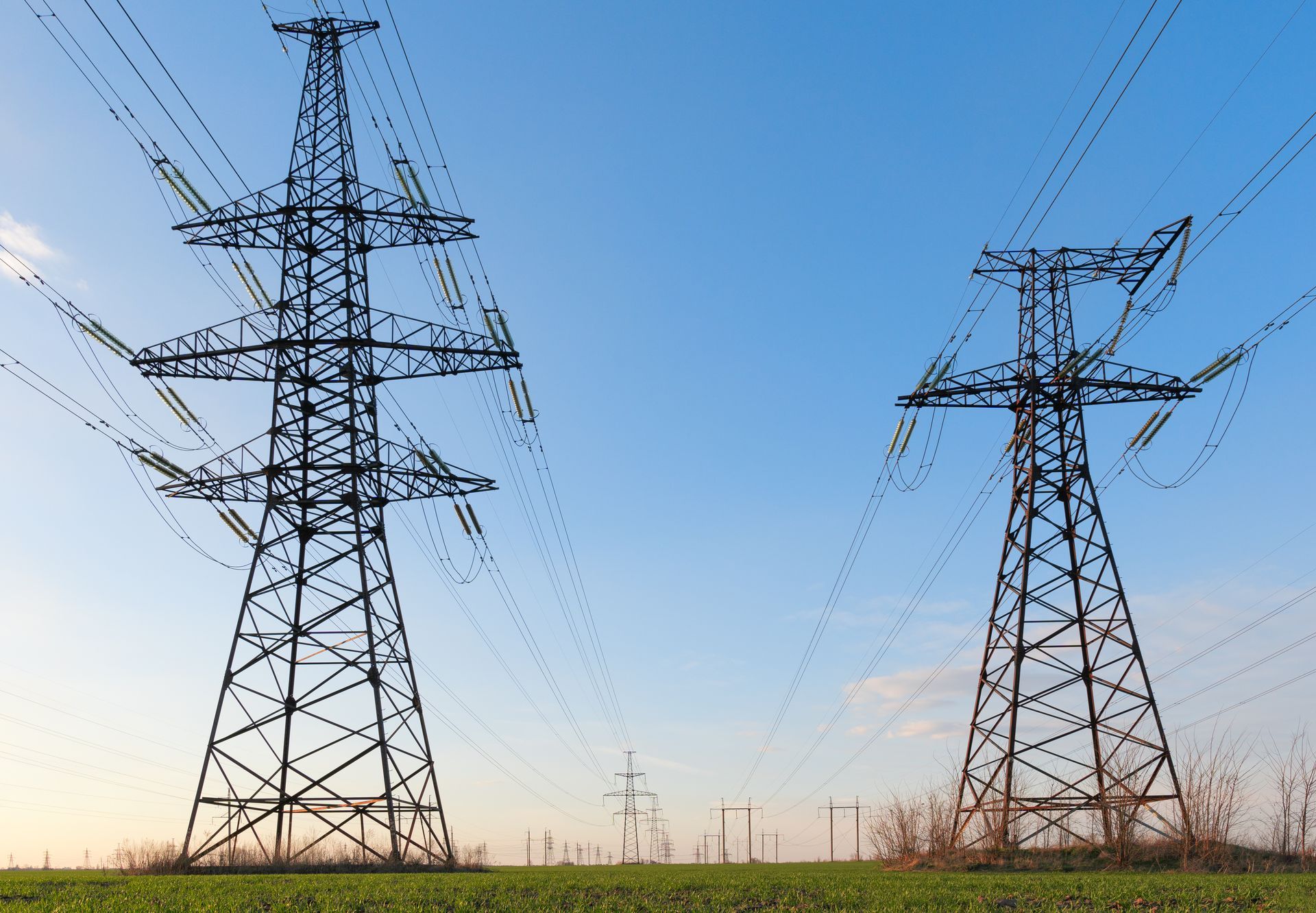 Two power lines in a field with a blue sky in the background.