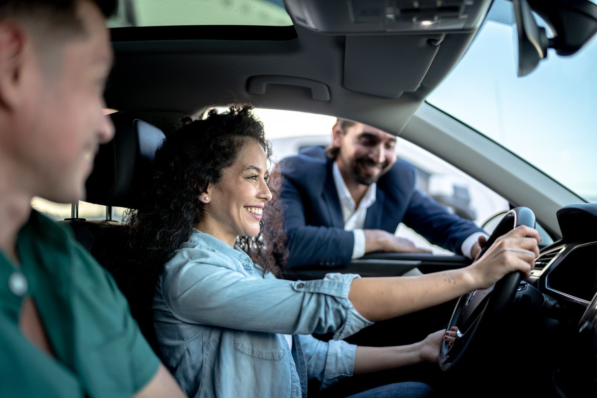 Donna sorridente mentre guida un'auto, sono presenti anche due uomini.