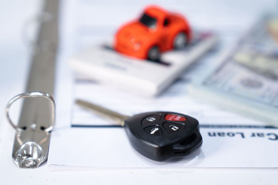 Chiave dell'auto sui documenti del prestito auto con macchinina giocattolo e denaro, a simboleggiare l'acquisto di un'auto.