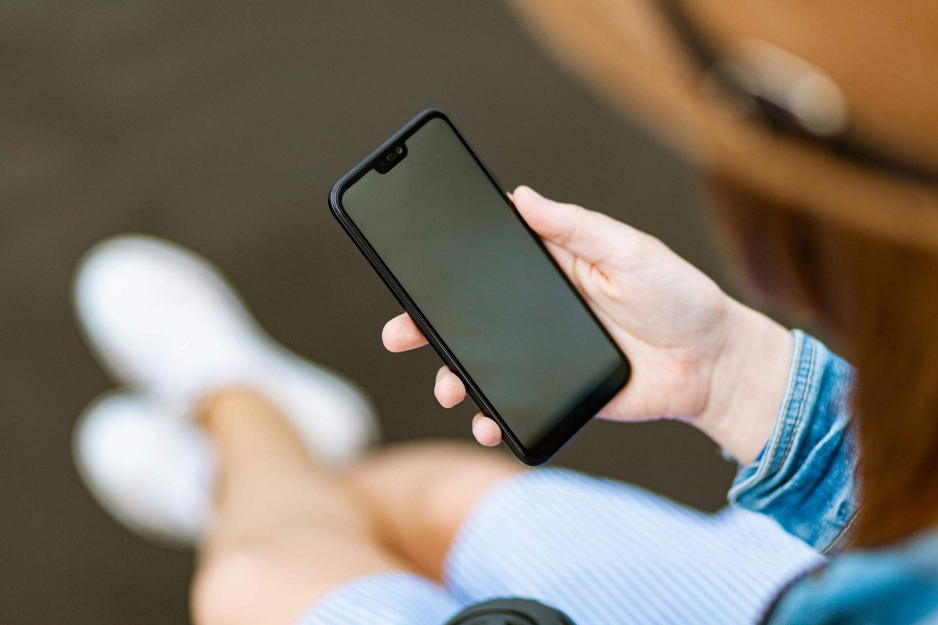 Eine Person sitzt im Freien und hält ein schwarzes Smartphone mit leerem Bildschirm in der Hand.