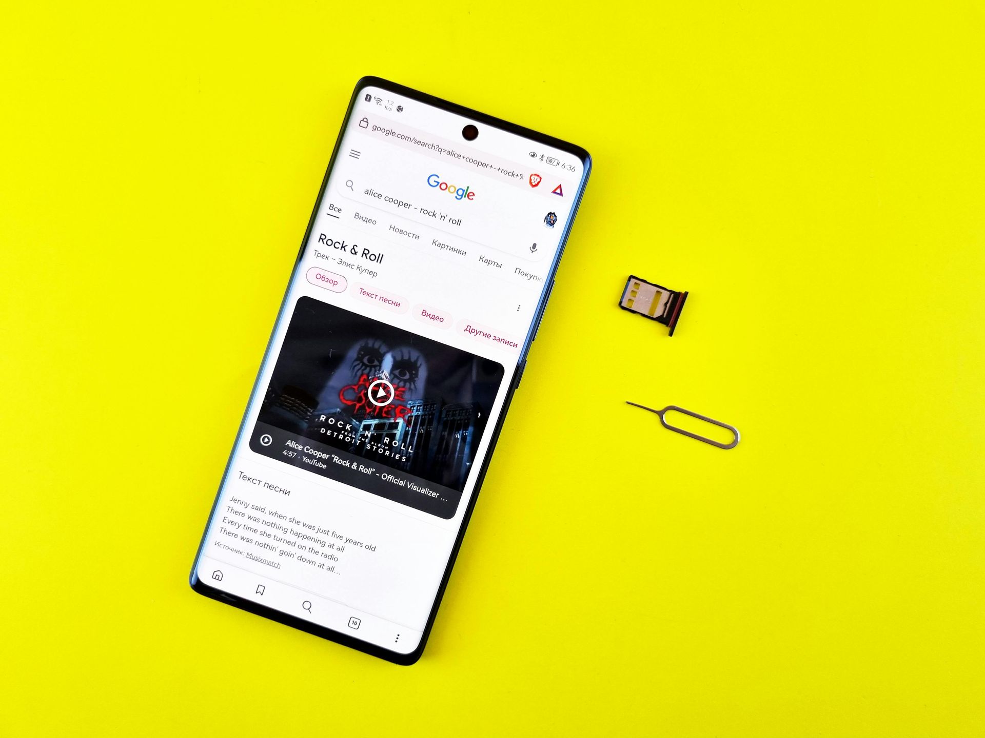 Auf einer gelben Oberfläche ist neben einem SIM-Kartenfach und einem Werkzeug ein Smartphone abgebildet, das ein Google-Suchergebnis anzeigt.