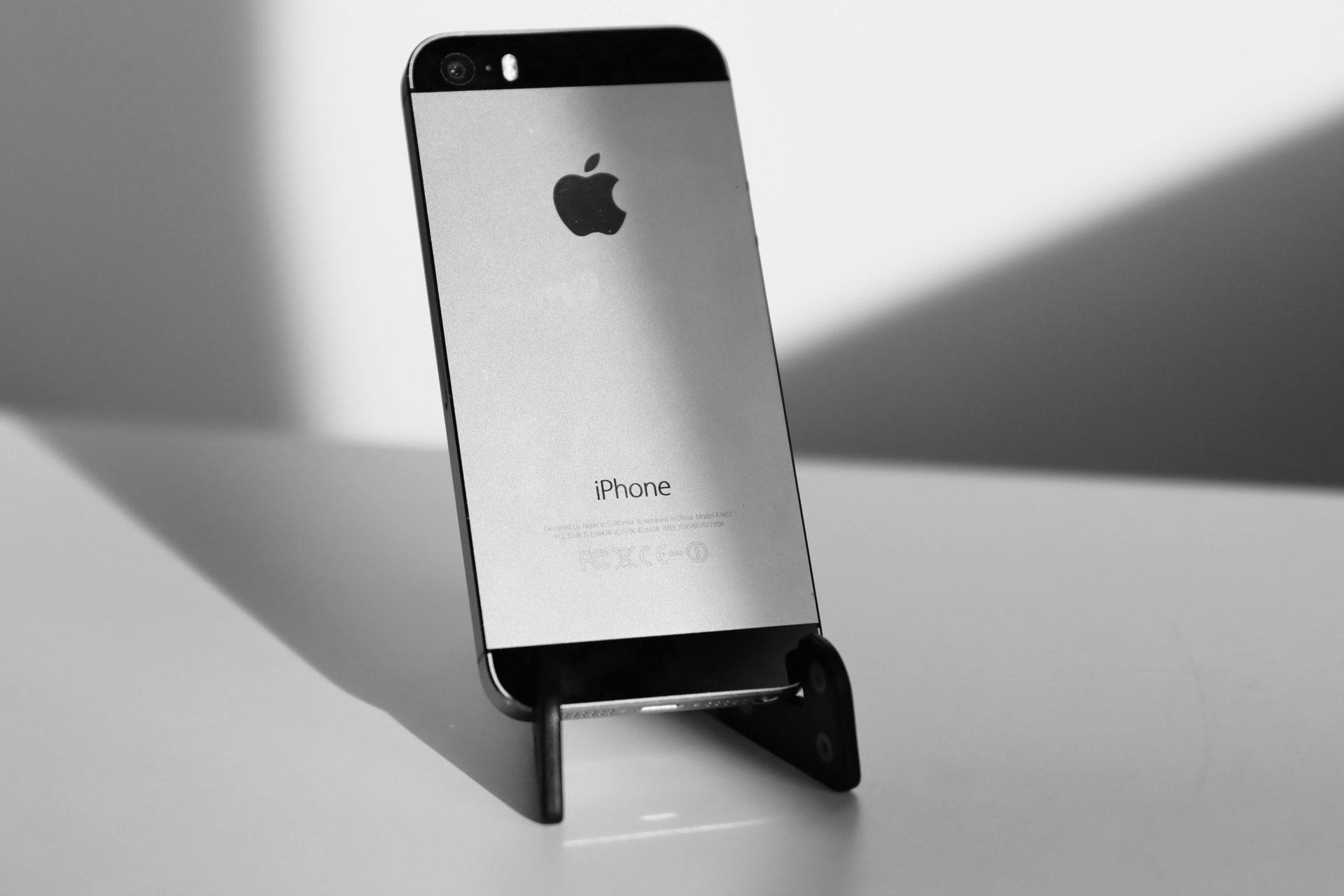 Ein iPhone ruht auf einem schwarzen Handyhalter, schräg im Schatten.