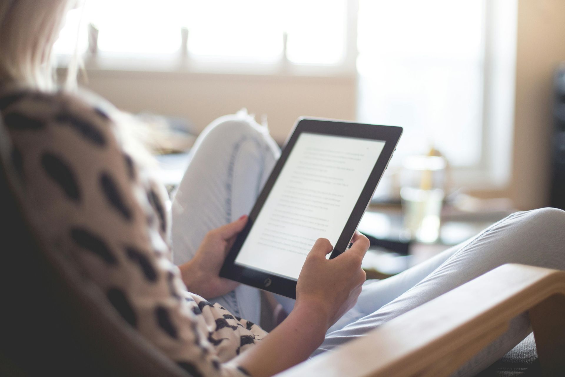 Frau sitzt und liest einen E-Reader. Innenbereich, natürliches Licht.