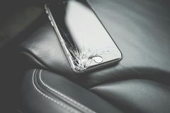 Ein gesprungener Smartphone-Bildschirm liegt auf einer schwarzen Lederoberfläche.