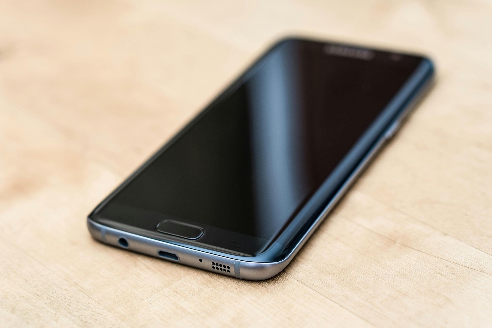 Schwarzes Smartphone auf hellem Holzgrund, schräge Ansicht.