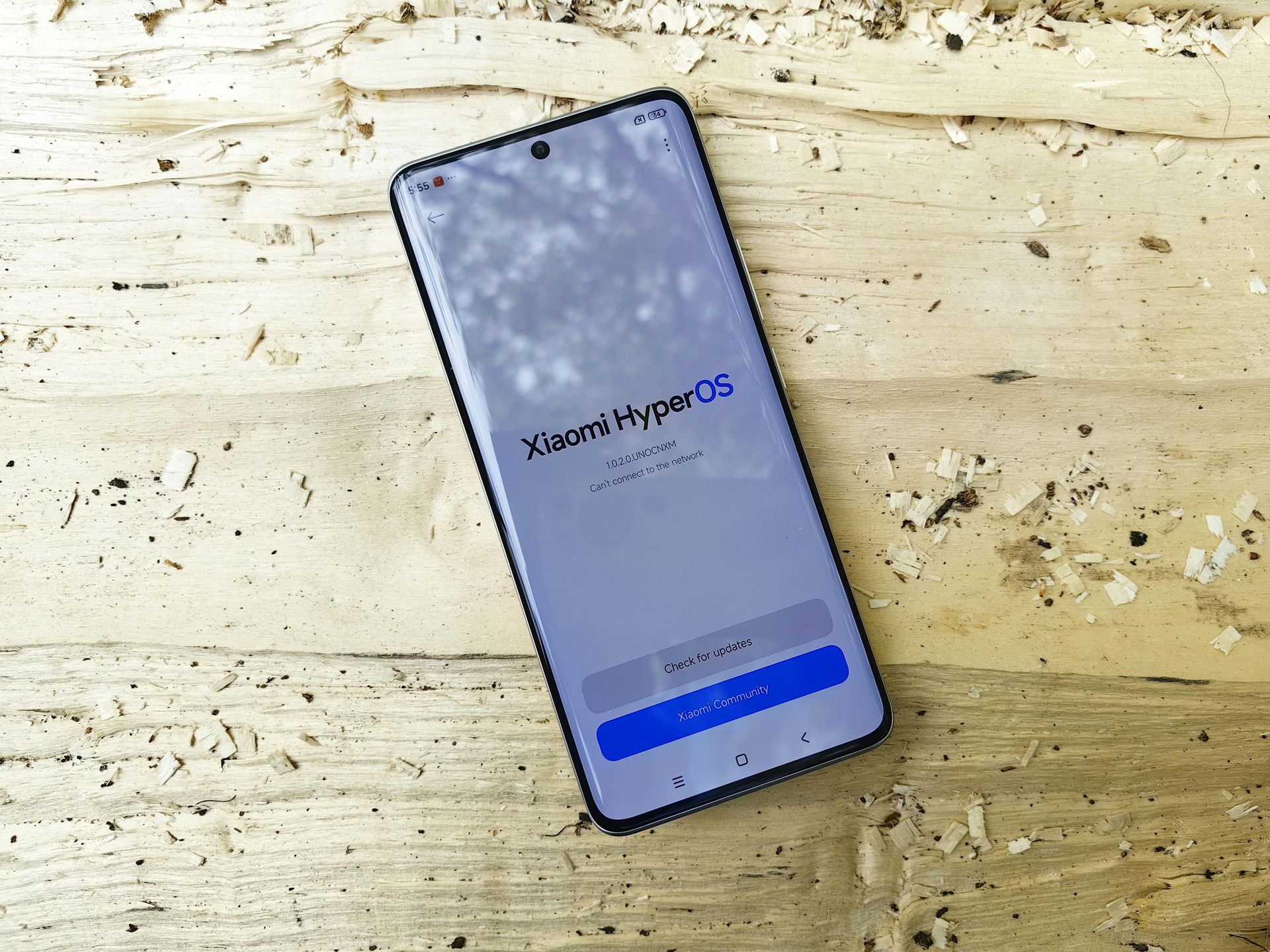Smartphone mit Xiaomi HyperOS-Logo auf einer Holzoberfläche.