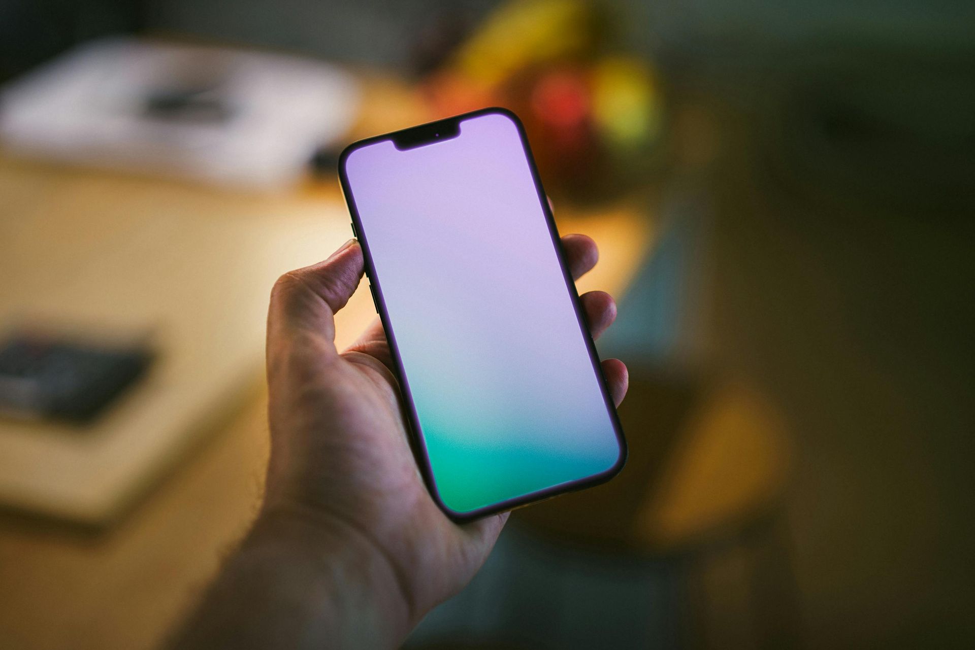 Hand hält Smartphone mit grün-violettem Farbverlaufsbildschirm.