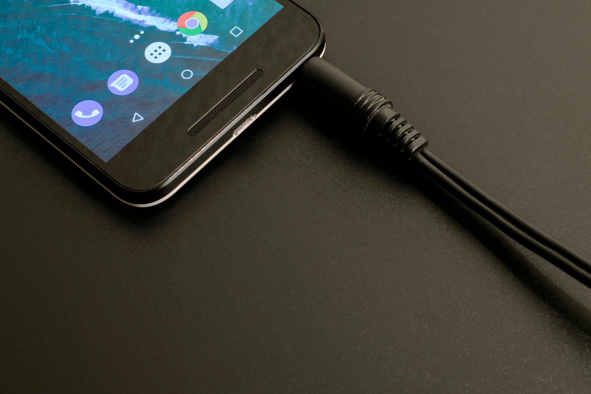 Schwarzes Smartphone mit angeschlossenem schwarzem Audiokabel, das auf einer schwarzen Oberfläche liegt.