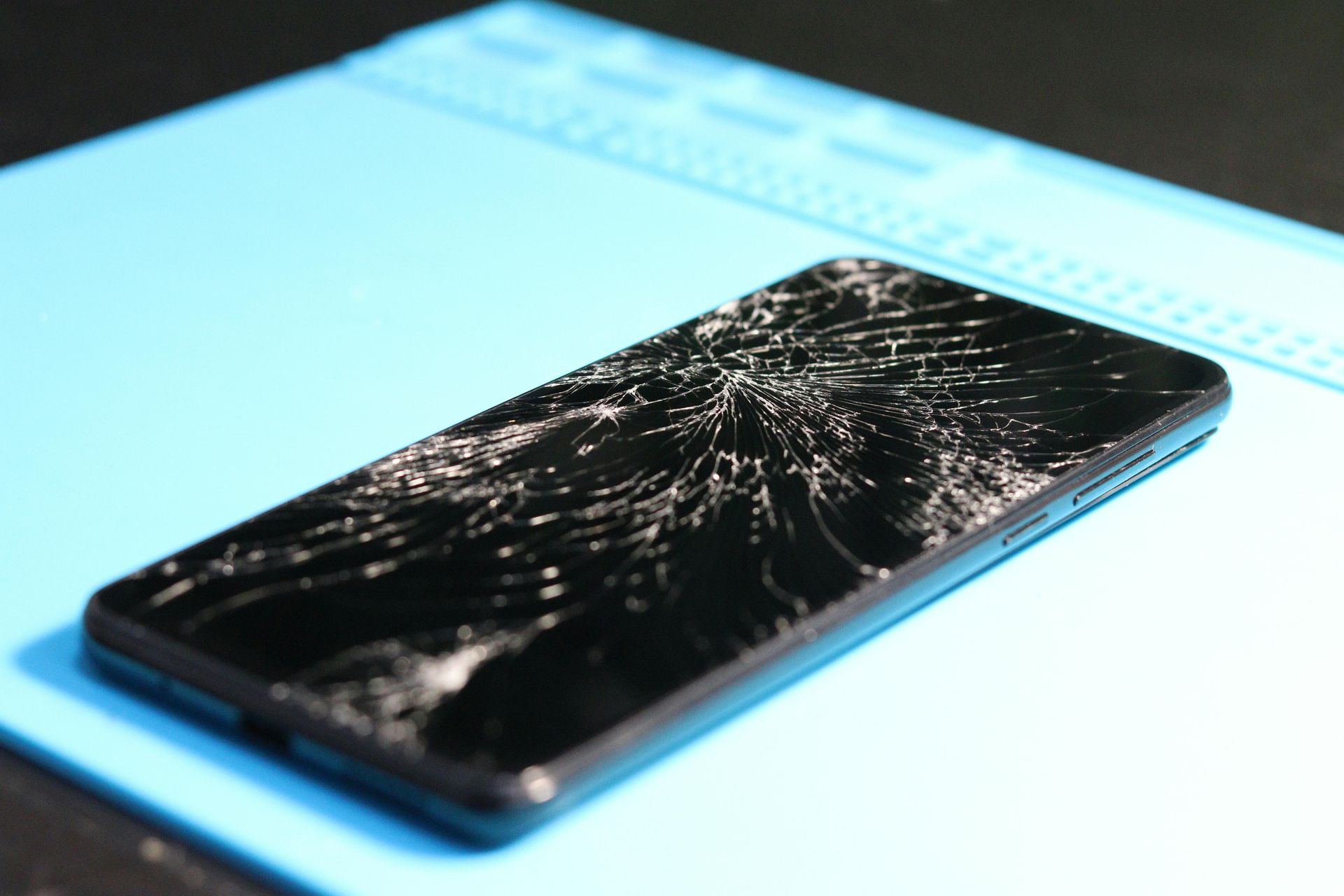 Ein gesprungener Smartphone-Bildschirm liegt auf einer blauen Matte und reflektiert das Licht.