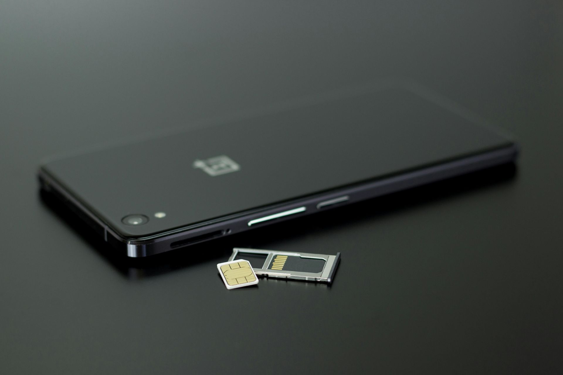 Schwarzes Smartphone mit SIM-Kartenfach und SIM-Karte auf dunkler Oberfläche.