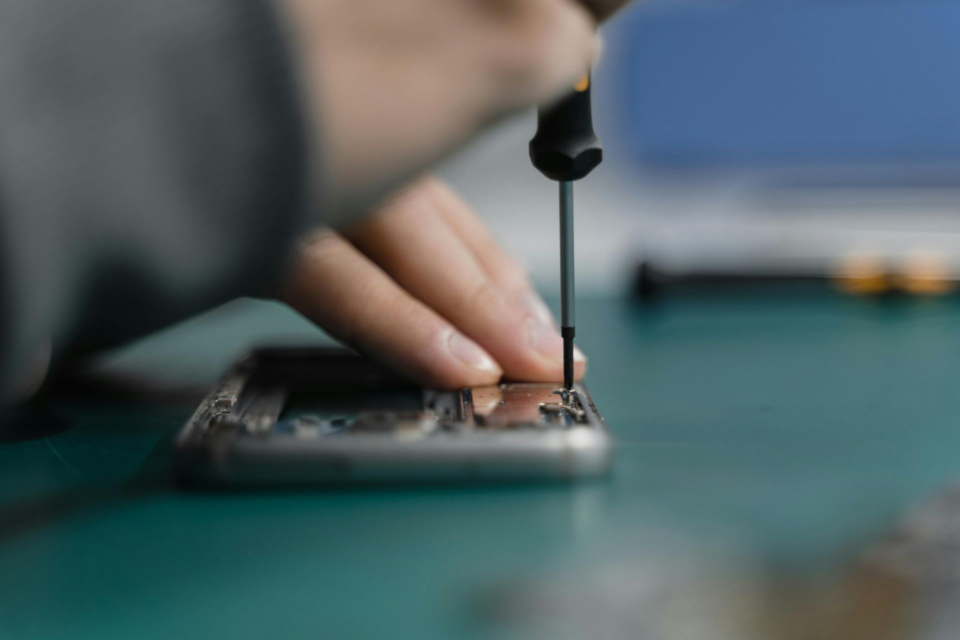 Eine Person repariert mit einem Schraubenzieher ein zerlegtes Smartphone auf einer grünen Matte.
