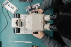 Eine Person betrachtet durch ein Mikroskop eine Handykomponente auf einer grünen Oberfläche.