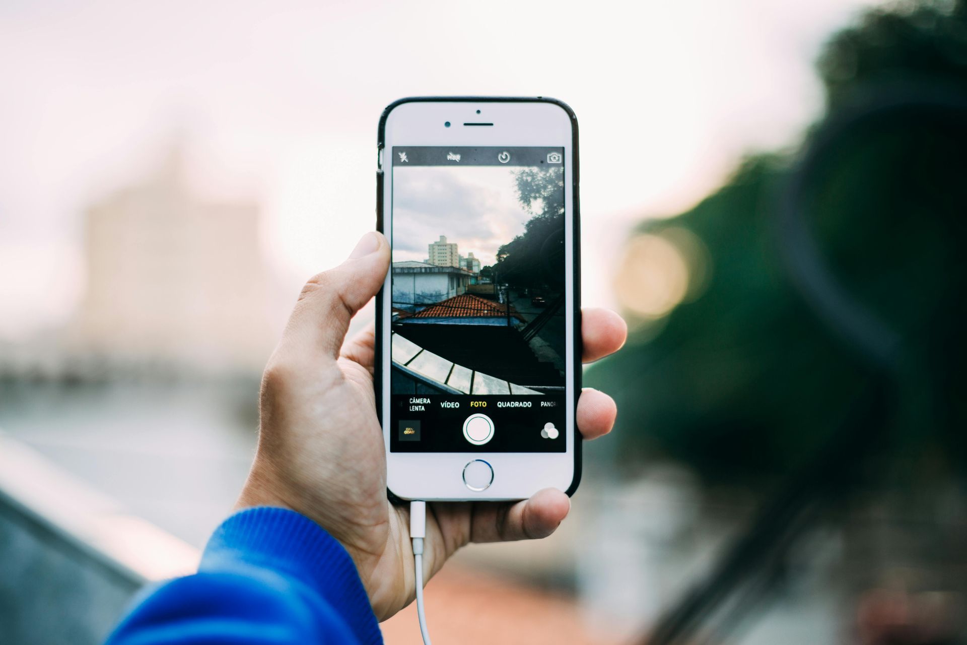 Eine Hand hält ein Smartphone und fotografiert im Freien ein Gebäude.